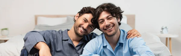 Позитивная молодая пара геев, обнимающая в спальне, баннер — стоковое фото
