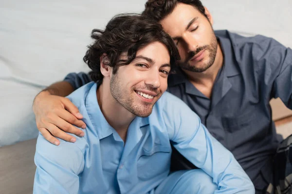 Complacido joven gay pareja abrazando en dormitorio - foto de stock