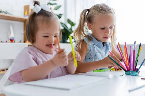 Mädchen nimmt rosa Bleistift in der Nähe verschwommenes behindertes Kind mit Down-Syndrom — Stockfoto