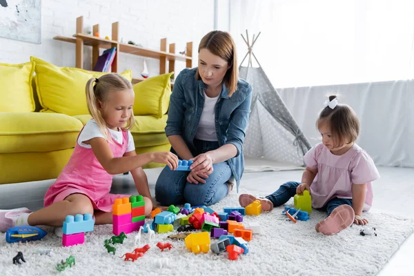 Kindergarten teacher playing building blocks with preschooler girl and toddler kid with down syndrome — Stock Photo