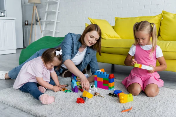 Professor de jardim de infância alegre jogando blocos de construção com menina pré-escolar e criança com síndrome de down — Fotografia de Stock