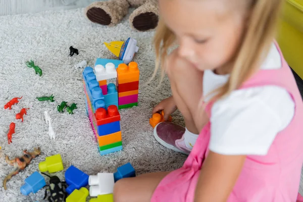 Fille floue en robe rose jouant blocs de construction sur le tapis dans la salle de jeux maternelle — Photo de stock