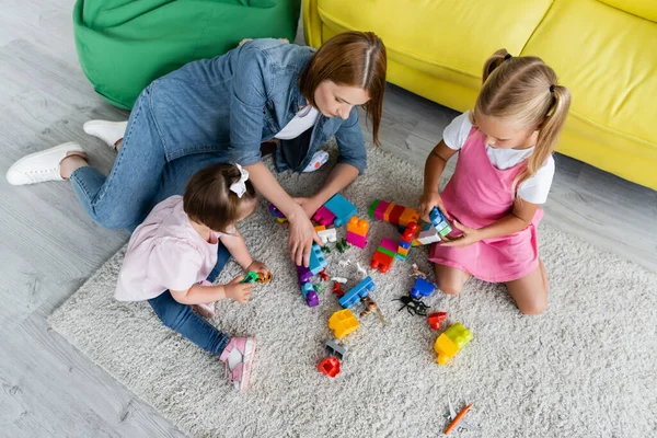 High angle view of kindergarten teacher playing building blocks with preschooler girl and toddler kid with down syndrome — Stock Photo