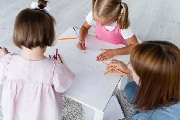 Hochwinkelaufnahme von Kindern, die in der Nähe von Kindergärtnerin auf Papier zeichnen — Stockfoto