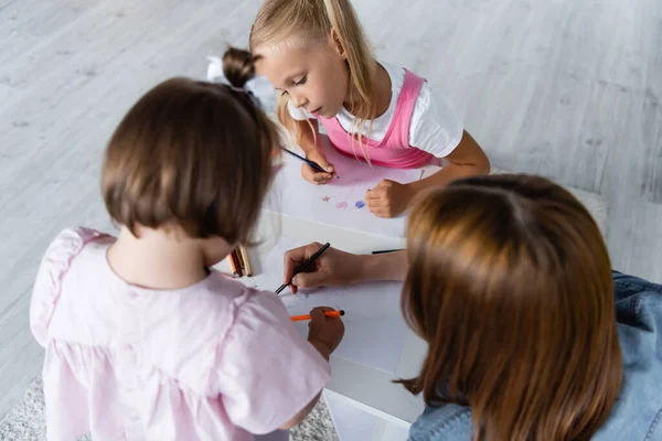 Vista ad alto angolo della ragazza bionda che guarda il disegno del bambino con sindrome di Down vicino all'insegnante di scuola materna — Foto stock