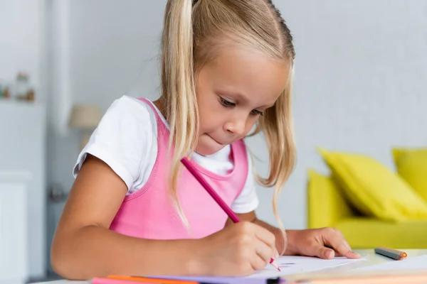 Blonde preschooler girl drawing with pink pencil on paper — Stock Photo