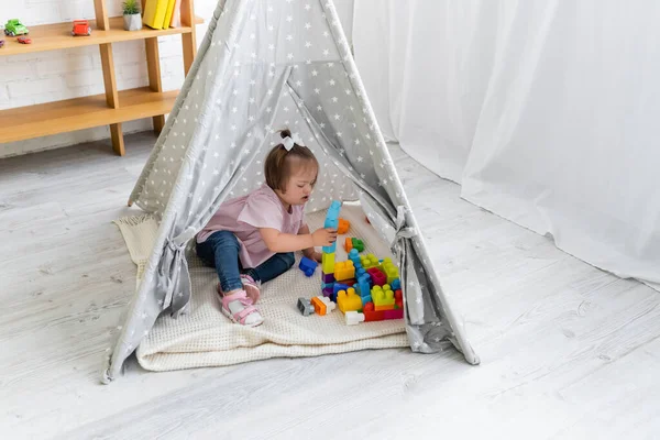 Kleinkind mit Down-Syndrom spielt Bausteine im Tipi-Zelt — Stockfoto