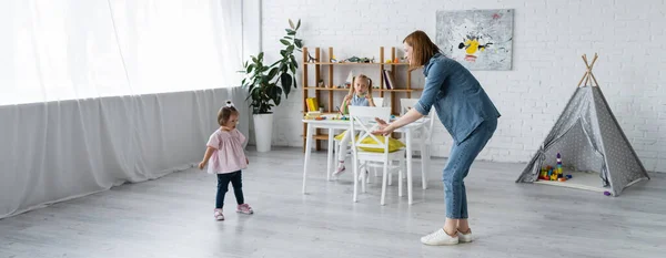 Maestro de jardín de infantes con las manos extendidas de pie cerca de un niño con síndrome de Down, pancarta - foto de stock