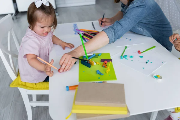 Professeur de maternelle atteignant la plasticine avec crayon près enfant handicapé — Photo de stock