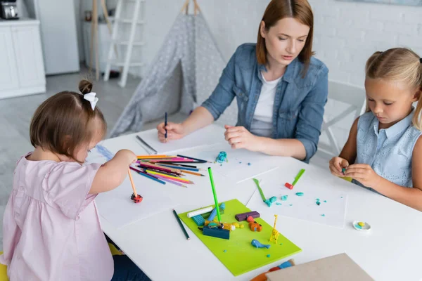 Enfant handicapé tenant crayon avec plasticine près de l'enseignant et la fille à la maternelle — Photo de stock