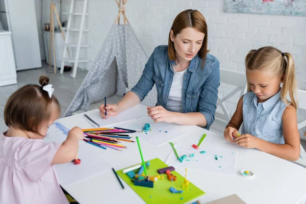 Verschwommenes und behindertes Kind hält Bleistift mit Knetmasse in der Nähe von Lehrerin und Mädchen im Kindergarten — Stockfoto