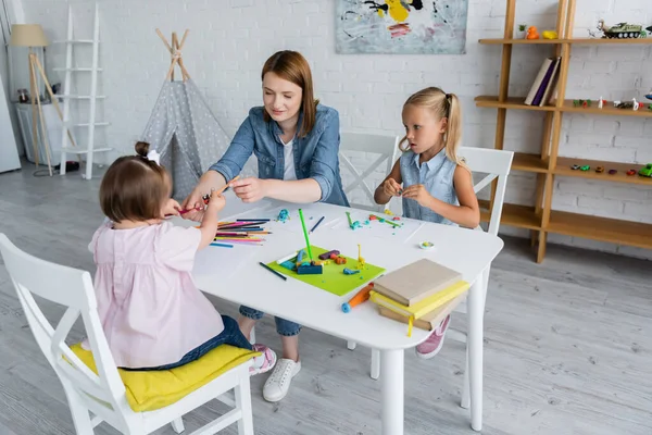 Professeur de maternelle donnant crayon à un enfant handicapé — Photo de stock