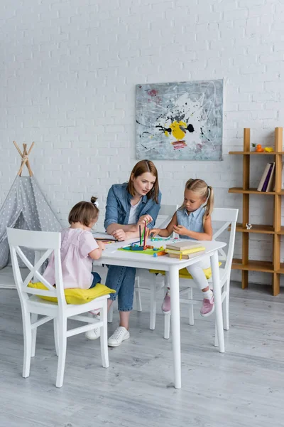 Maestro de jardín de infantes feliz mirando niño preescolar moldeado plastilina cerca de niño discapacitado con síndrome de Down - foto de stock