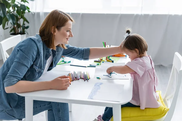 Happy kindergarten teacher reaching disabled child with down syndrome molding plasticine on paper — Stock Photo