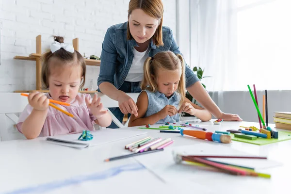 Teacher near preschooler girl and disabled child with down syndrome molding plasticine in private kindergarten — Stock Photo