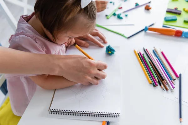 Enseignant aidant fille handicapée avec le dessin du syndrome du duvet dans la maternelle privée — Photo de stock