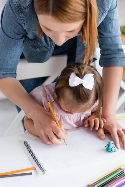 Vista ad alto angolo di insegnante che assiste ragazza disabile con sindrome di Down disegno nella scuola materna privata — Foto stock