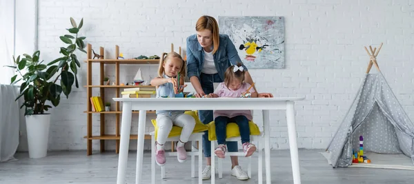 Insegnante in piedi dietro la ragazza in età prescolare e bambino disabile con sindrome di Down disegno in asilo privato, banner — Foto stock