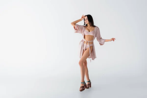 Full length of joyful young woman posing in underwear and silk robe on white — Stock Photo