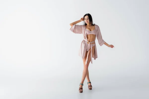Full length of smiling young woman posing in underwear and silk robe on white — Stock Photo