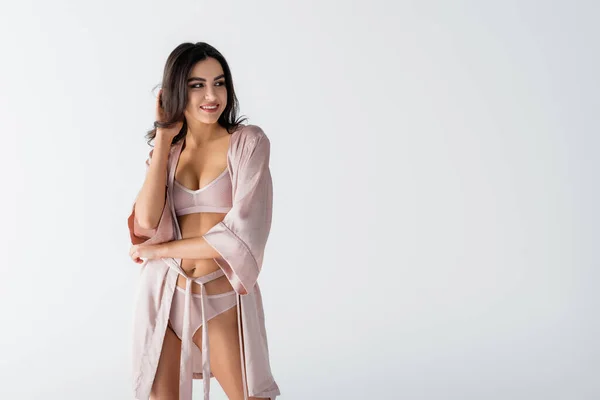 Felice giovane donna in biancheria intima e vestaglia di seta guardando lontano isolato su bianco — Foto stock