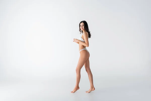 Piena lunghezza di giovane donna a piedi nudi in lingerie che cammina su bianco — Foto stock