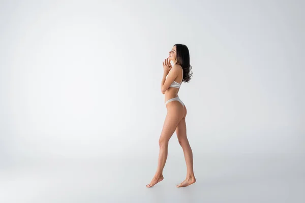 Longitud completa de joven descalza y alegre mujer en lencería caminando sobre blanco - foto de stock