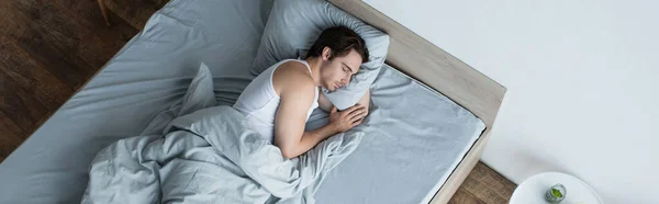 Vista de ángulo alto del hombre joven durmiendo en la almohada debajo de la manta azul, bandera - foto de stock