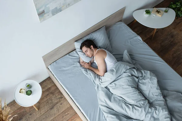 Vista de ángulo alto de hombre joven durmiendo bajo manta azul - foto de stock