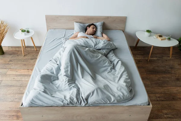 Молодой человек, спящий на синем постельном белье возле тумбочек — стоковое фото
