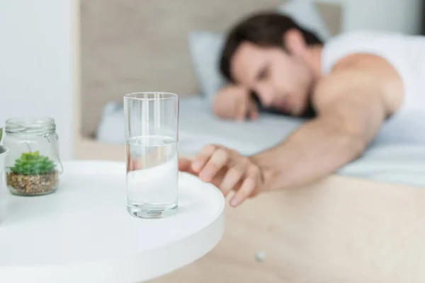 Verschwommener Mann greift nach Wasserglas, während er im Bett liegt — Stockfoto