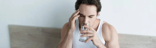Kranker Mann berührt Kopf und trinkt Wasser, während er an Migräne leidet, Banner — Stockfoto