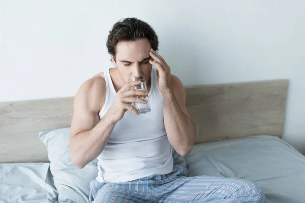 Молодий чоловік п'є воду з закритими очима, страждаючи від головного болю — стокове фото