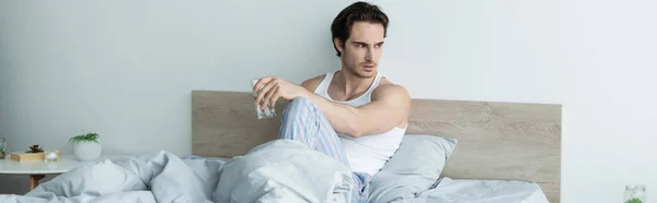 Hombre deprimido mirando hacia otro lado mientras está sentado en la cama con un vaso de agua, pancarta - foto de stock