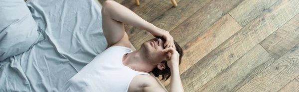 Vue grand angle de l'homme couvrant les yeux avec les mains tout en étant couché sur le lit le matin, bannière — Photo de stock