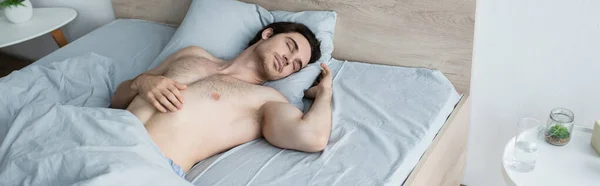 Hombre sin camisa durmiendo en la cama cerca de un vaso de agua en la mesita de noche, pancarta - foto de stock