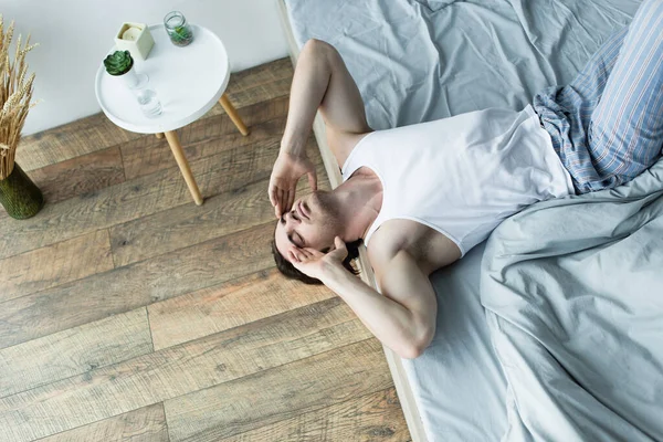 Vista de ángulo alto del hombre acostado en el borde de la cama mientras sufre de resaca en la mañana - foto de stock