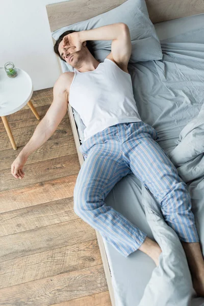 Vista de ángulo alto del hombre enfermo acostado en el borde de la cama con la mano cerca de la cara - foto de stock