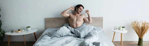 Щасливий чоловік розтягується закритими очима, сидячи в ліжку, банер — стокове фото