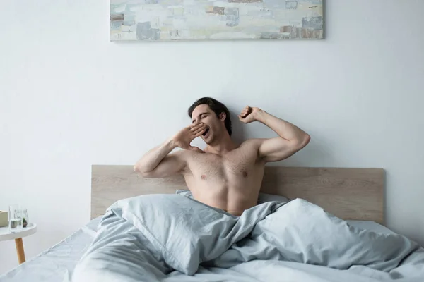 Сонный мужчина растягивается и зевает с закрытыми глазами по утрам — стоковое фото