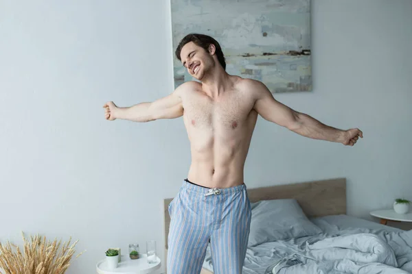 Hemdloser Mann in Pyjamahose lächelt und dehnt sich im Schlafzimmer — Stockfoto