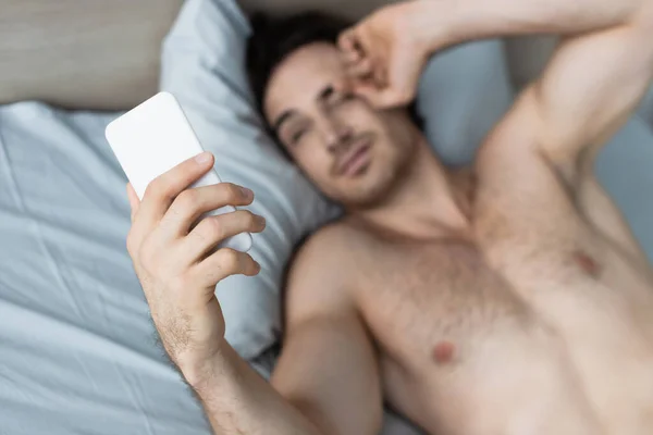 Visão de alto ângulo do homem borrado esfregando os olhos enquanto olha para o smartphone de manhã — Fotografia de Stock