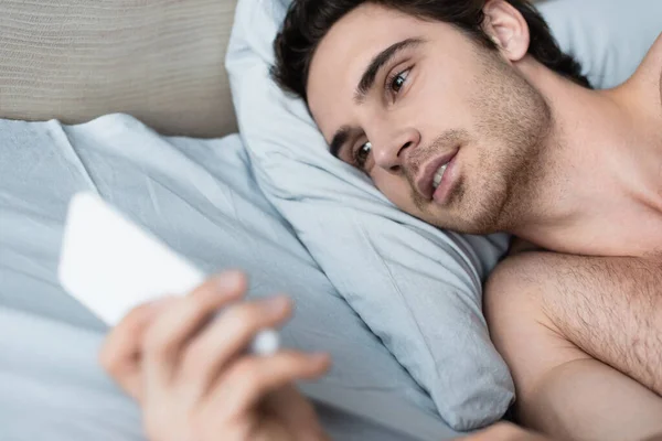 Hombre acostado en la cama y usando un teléfono móvil borroso - foto de stock