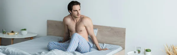 Morena sin camisa hombre mirando hacia otro lado mientras está sentado en la cama, pancarta - foto de stock