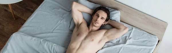 Vue grand angle de l'homme torse nu couché dans le lit avec les mains derrière la tête, bannière — Photo de stock