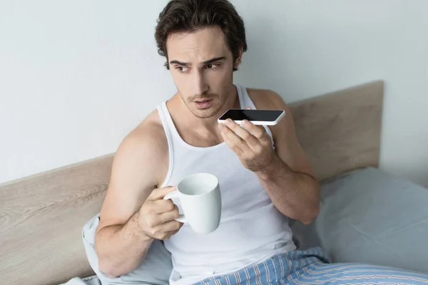Молодой человек отправляет голосовое сообщение, держа чашку кофе — стоковое фото