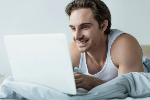 Glücklicher junger Mann blickt auf Laptop im Bett — Stockfoto