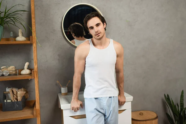 Young man in white tank top looking at camera in bathroom — Stock Photo