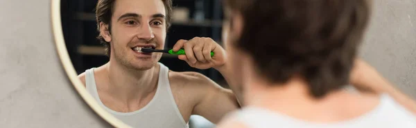 Young man brushing teeth near mirror in bathroom, banner — Stock Photo