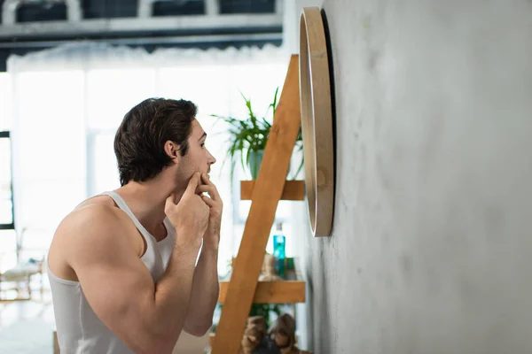Seitenansicht eines brünetten Mannes, der Pickel im Gesicht in der Nähe des Spiegels quetscht — Stockfoto